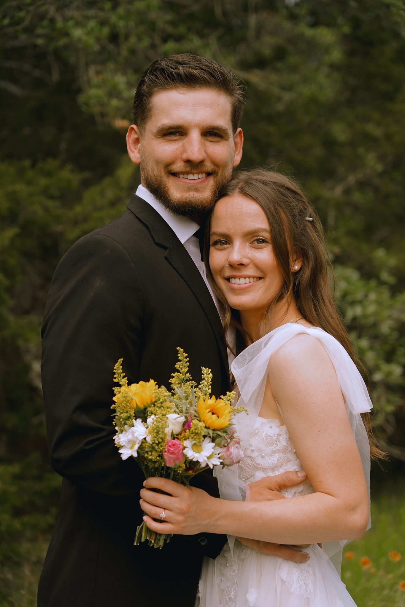 Wedding couple holding colorful bouquet while posing outdoors.