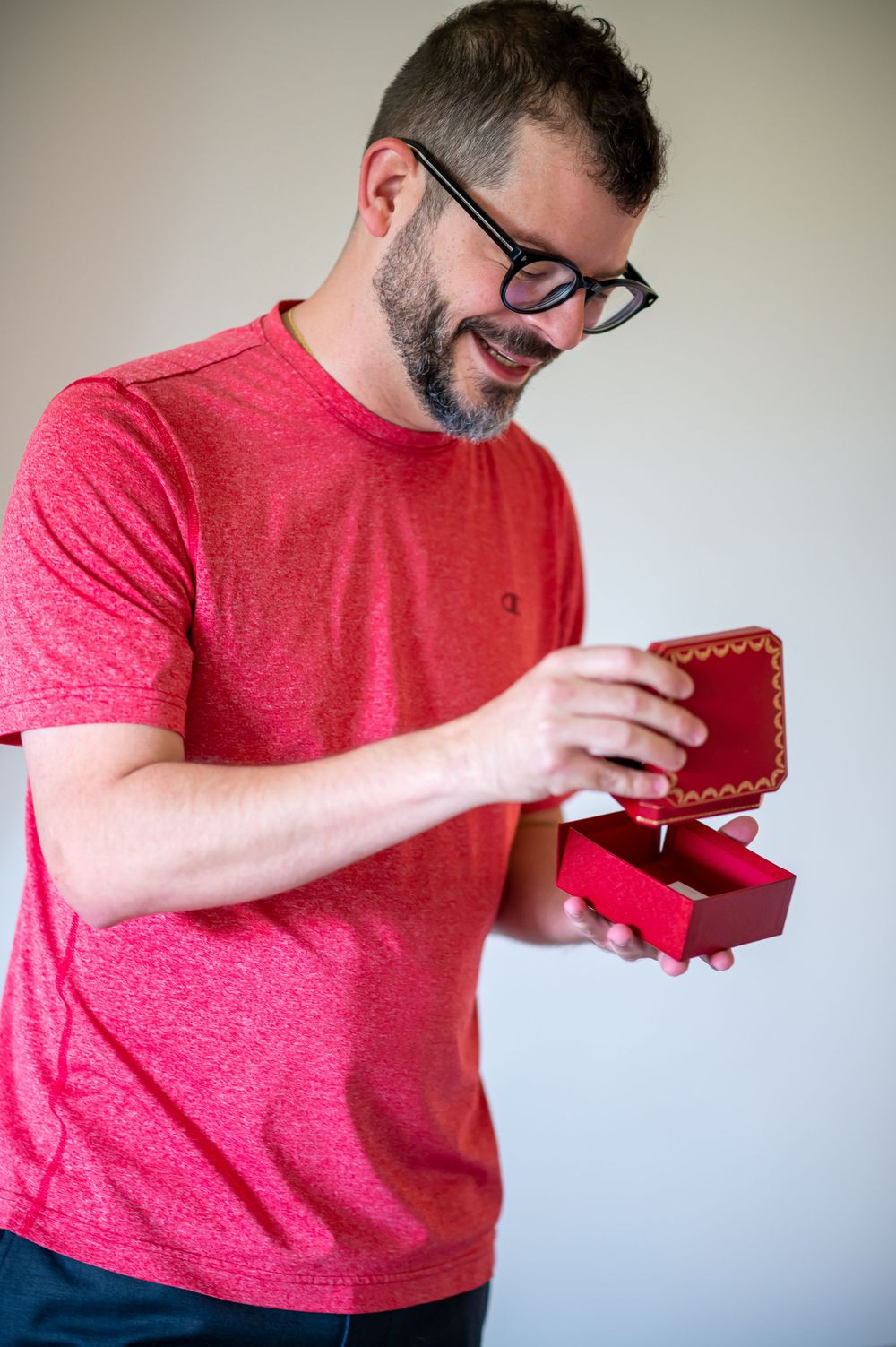 Person in red t-shirt opening small red gift box with excitement.