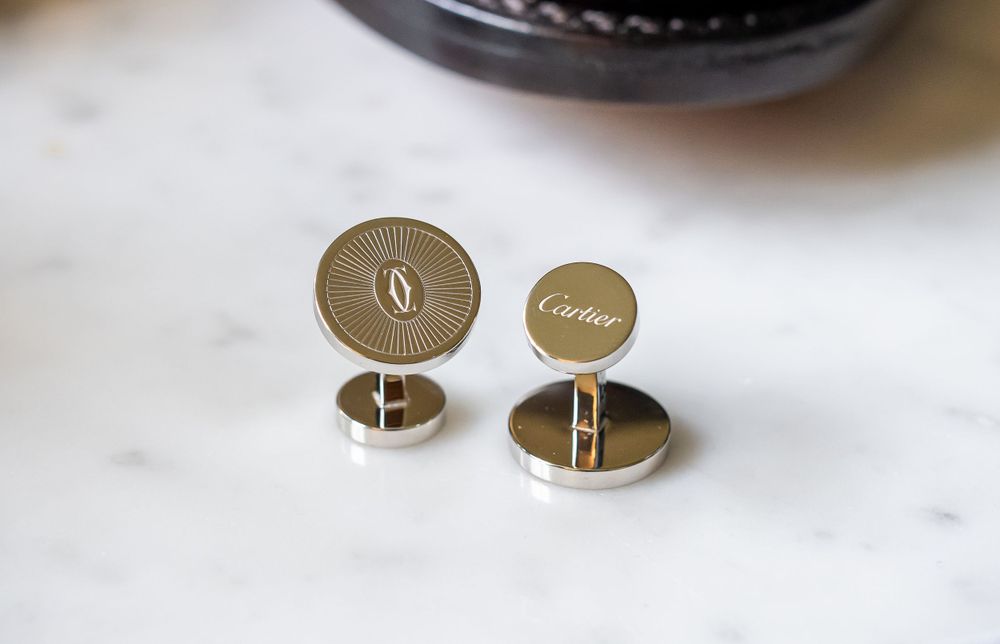 Close-up of gold monogrammed cufflinks on white marble surface.