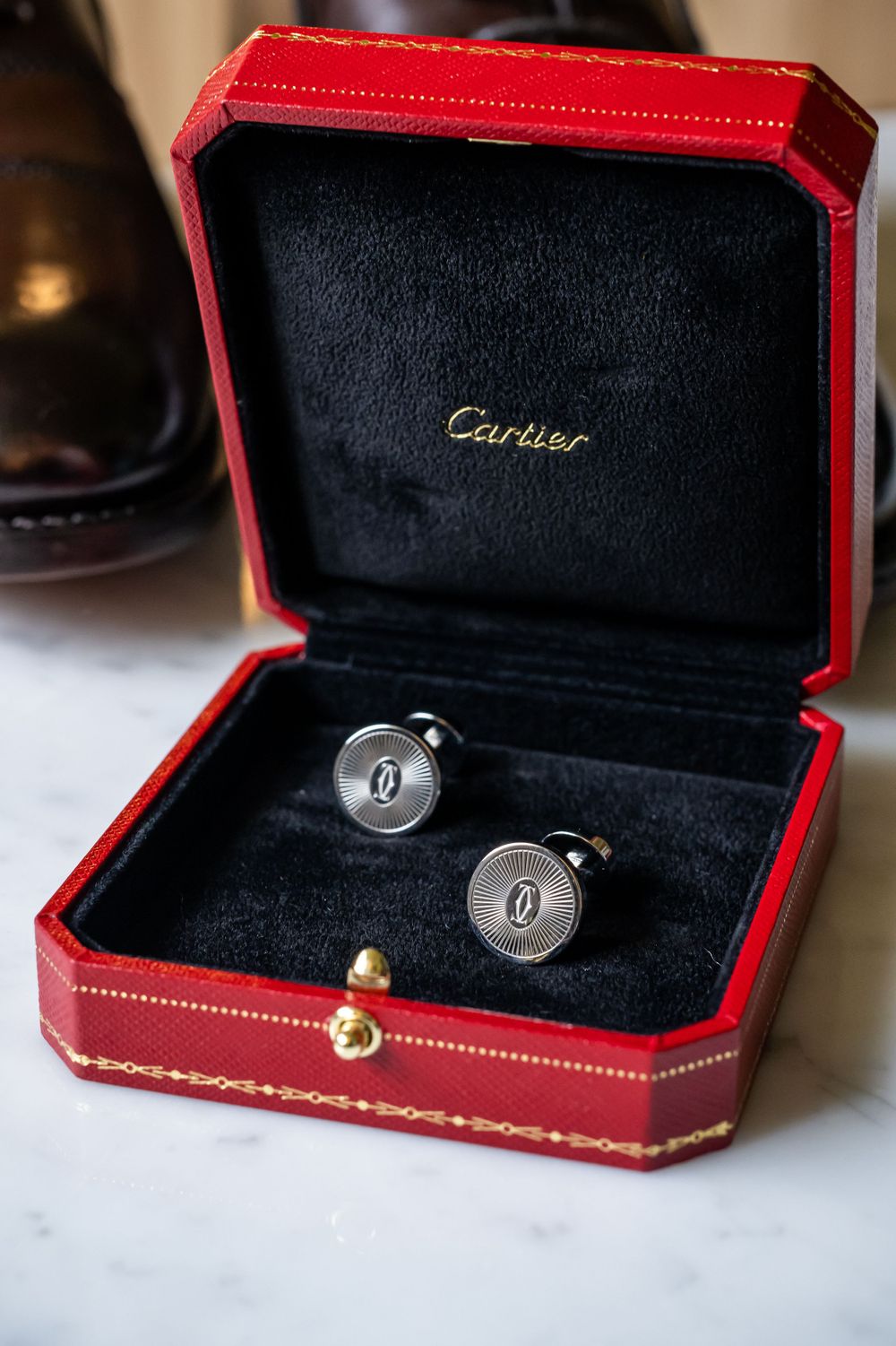 Cartier cufflinks displayed in red leather presentation box on marble surface.