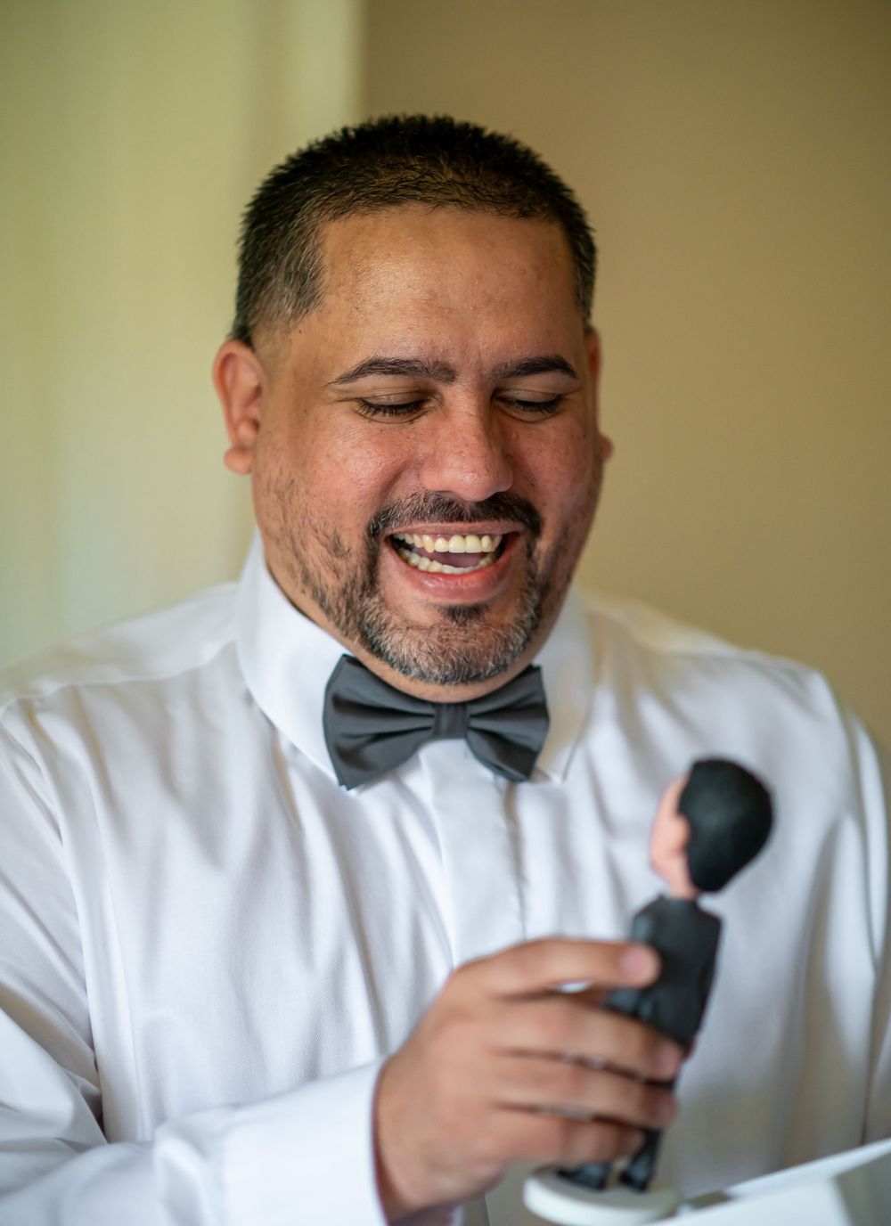 Person in white dress shirt and bow tie smiling while holding a small figurine.