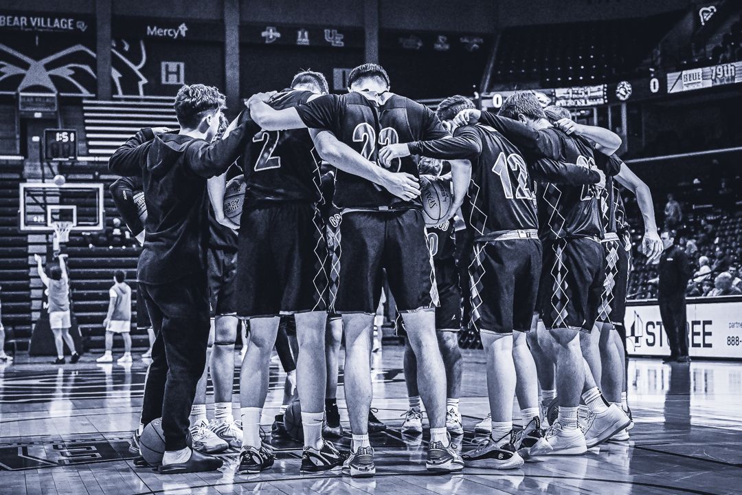 Basketball team huddles together in unity before a game in black and white photography.