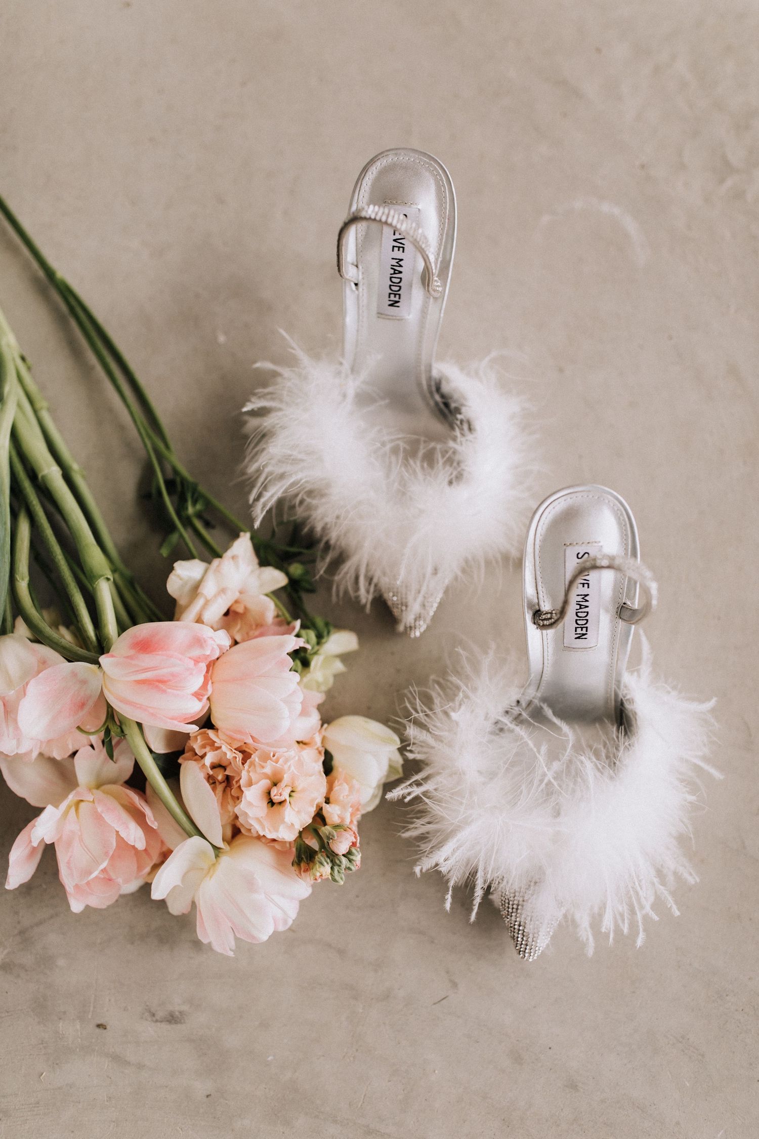 White fluffy feather heels styled with soft pink roses on a neutral beige surface.