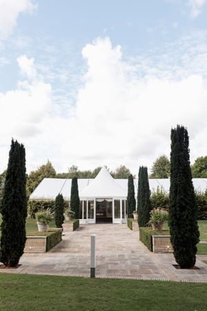 Elegant outdoor wedding venue with white pavilion and cypress trees lining a stone patio.