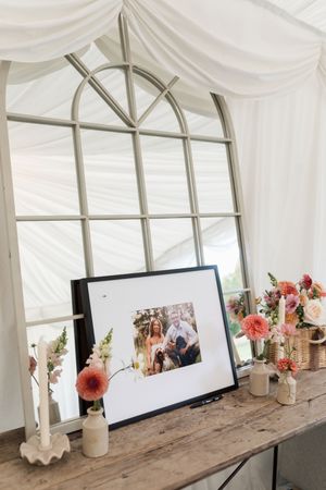 Wedding photos displayed on screens in a white tent with floral decorations and rustic wooden tables.
