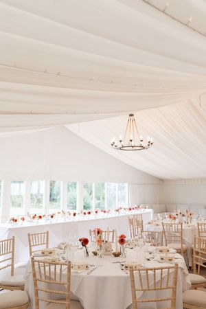 An elegant white wedding reception tent with round tables and chiavari chairs.