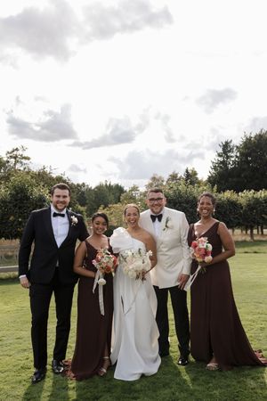 Wedding party in formal black and brown attire posing outdoors on a cloudy day.