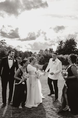 Wedding party in black and white formal attire posing outdoors under cloudy skies in a grassy field.