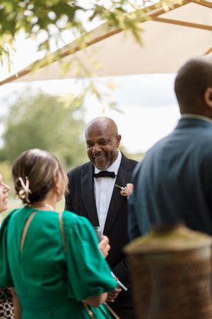 Guests mingle and converse during an elegant outdoor wedding reception under a white tent canopy.