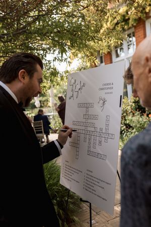 Wedding guests gather around a crossword puzzle activity board at an outdoor reception.