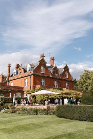 Elegant red brick Victorian manor house with manicured lawn and outdoor seating area under a bright blue sky.