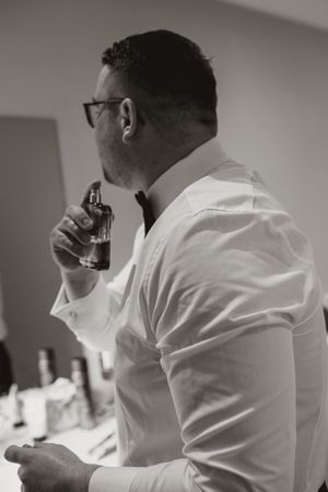 Side profile of someone in a white dress shirt taking a sip from a glass during wedding preparations.