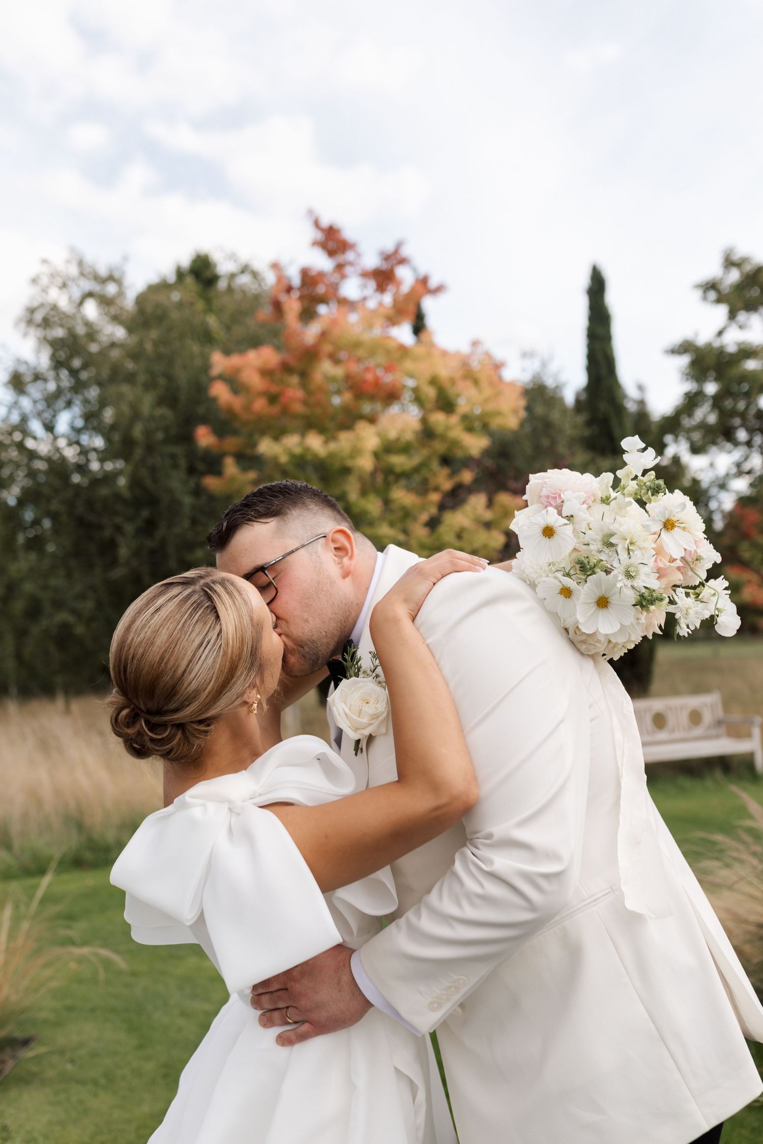 A romantic wedding moment captured in a garden with tall grasses and fall colors in the background.