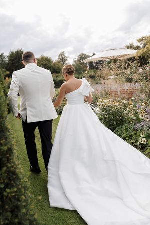 A flowing white wedding dress train trails behind on a garden path.