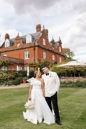 A couple shares romantic moments on a lush green lawn with a beautiful brick mansion in the background.