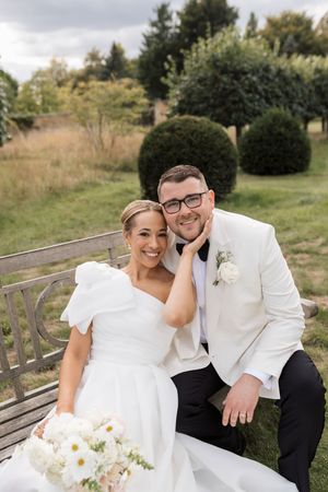 A couple shares intimate moments on a wooden bench during their wedding photoshoot outdoors.