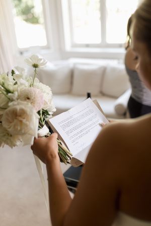 Wedding preparation moment with floral bouquet and paper in hand.