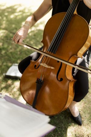 Classical cello being played outdoors with warm wooden tones in natural lighting.