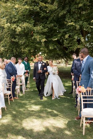Outdoor wedding ceremony setup with white chairs on a grassy lawn under trees.