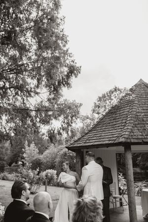 Wedding guests gathering under a rustic wooden gazebo.