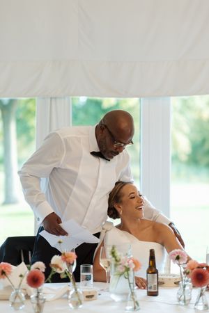 A candid moment captured during a wedding reception with floral centerpieces and natural window light.