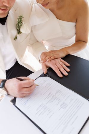 Close up view of couple signing marriage documents with white flowers and greenery.