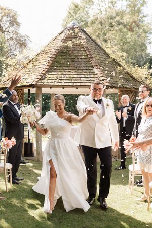 Wedding guests at an outdoor garden reception playfully hold up white laundry on clotheslines between gazebos.