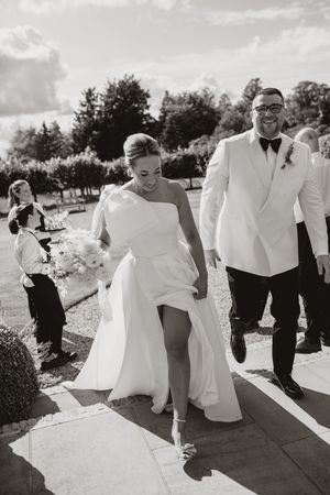 Wedding party walks and laughs together on sunny pathway during outdoor celebration.