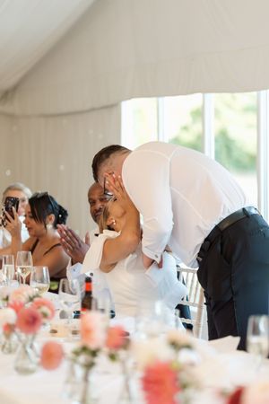 Wedding guests laugh together at reception tables decorated with floral centerpieces.