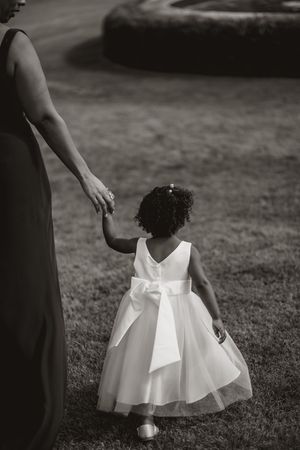 A young flower girl in a white dress twirls on the grass during an outdoor event.