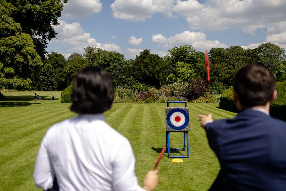 Wedding guests enjoying outdoor lawn games with a target practice setup on a sunny summer day.