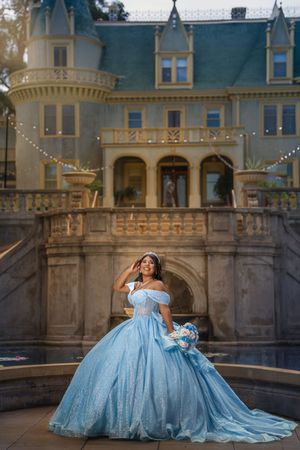 A flowing light blue ballgown dress photographed in sequence against an elegant castle-like architectural backdrop at sunset.