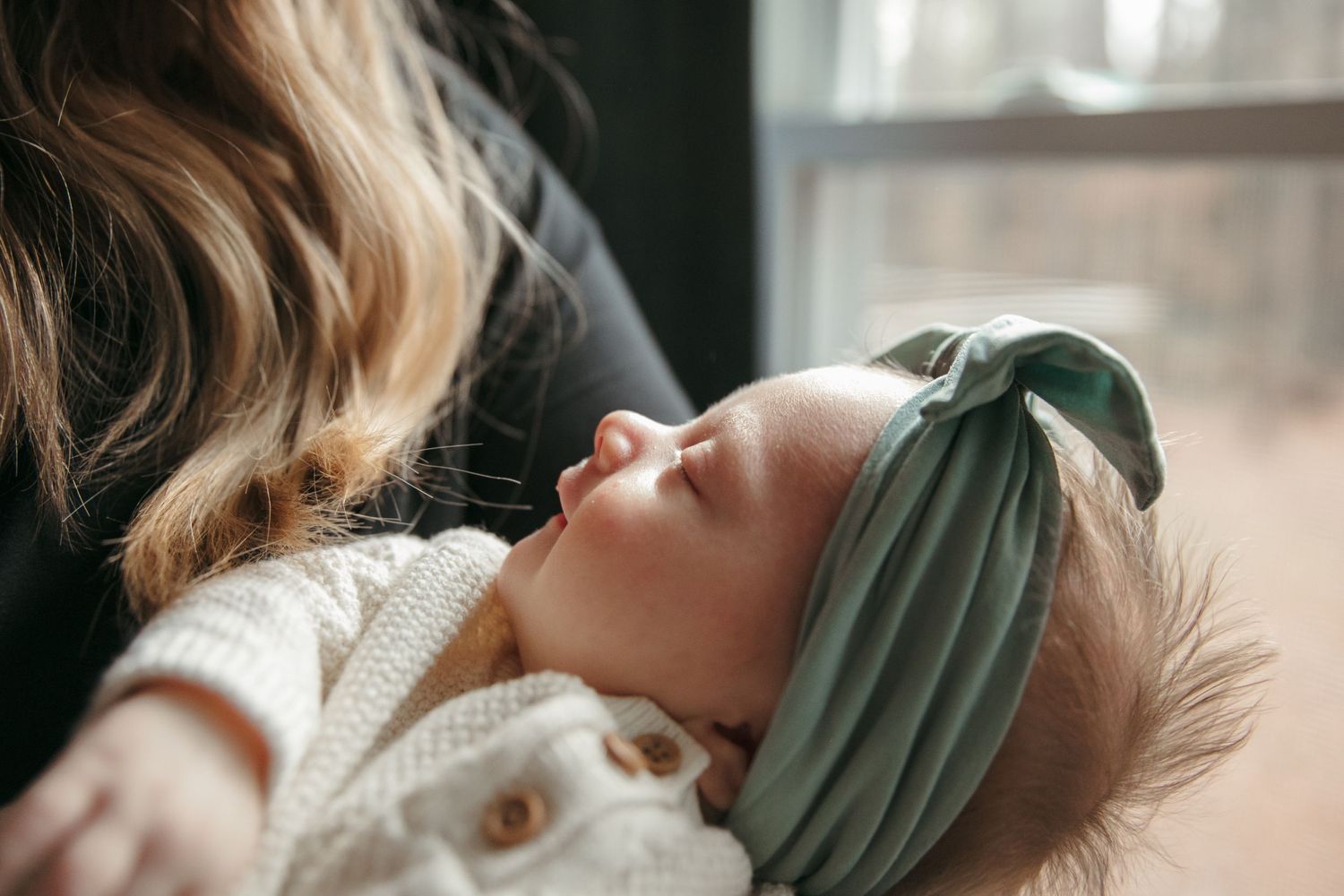 A serene close-up of a newborn with a headband that is soft textured fabrics in muted tones.