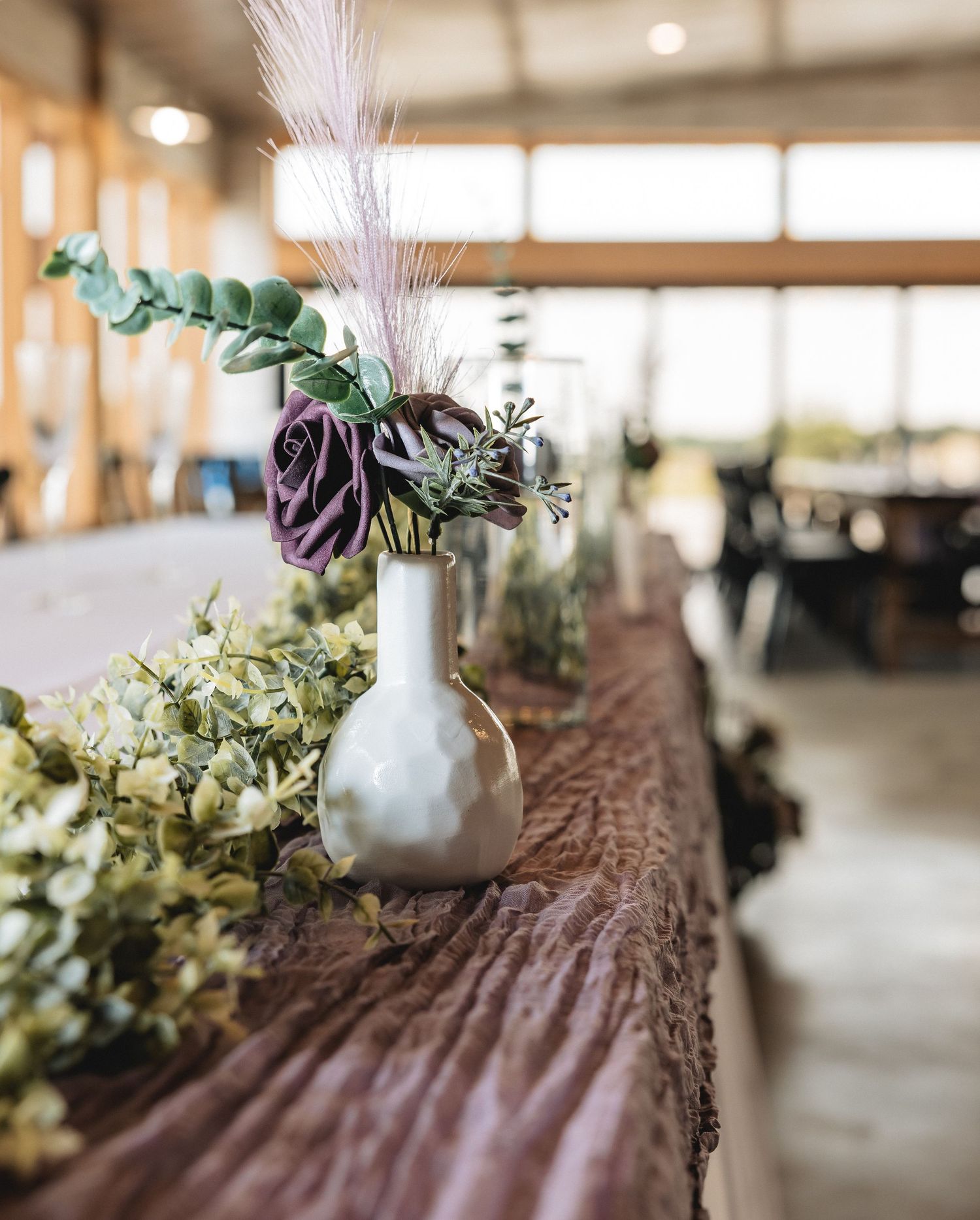 Wedding table decor features delicate peach roses and eucalyptus leaves arranged around elegant gold-rimmed place settings.