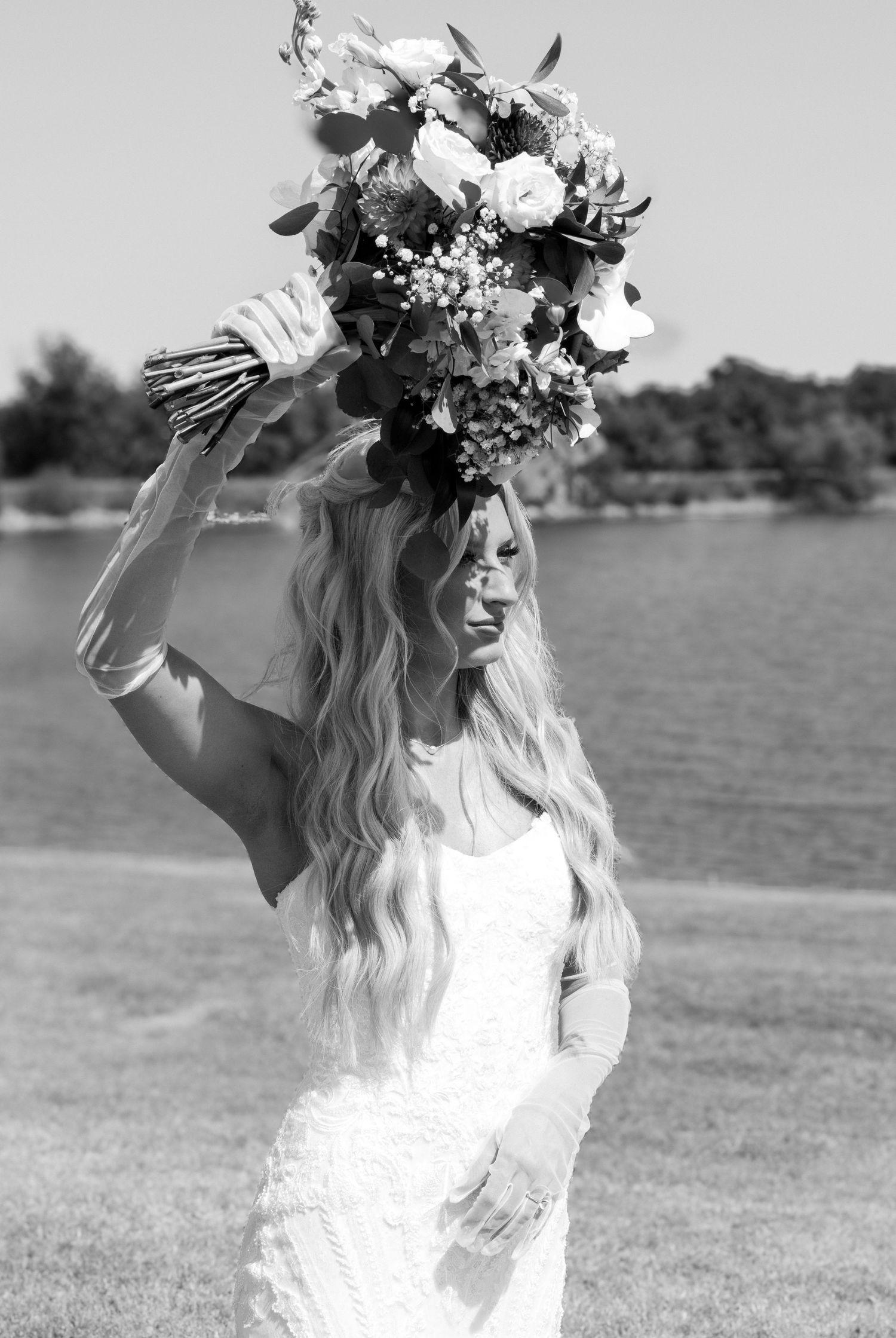 Black and white photo of bride holding bouquet overhead in an elegant lace dress.