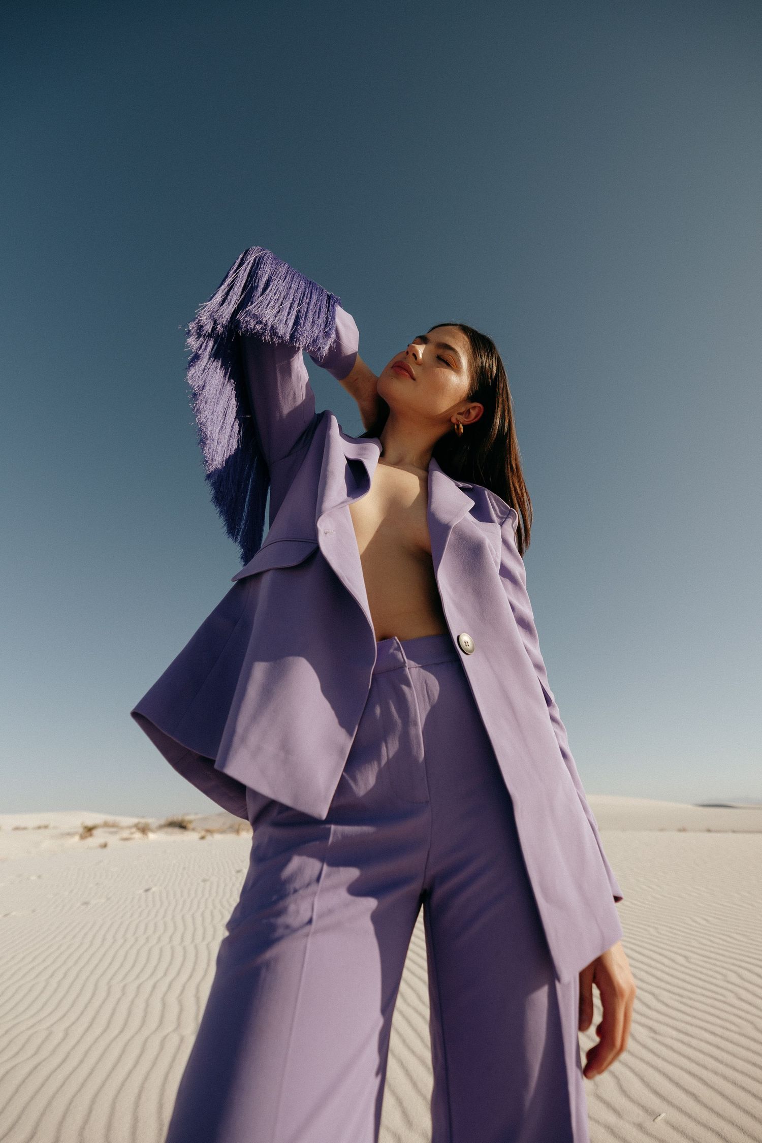 Fashion photo of a model in a lavender suit posing dramatically against sand dunes and blue sky.