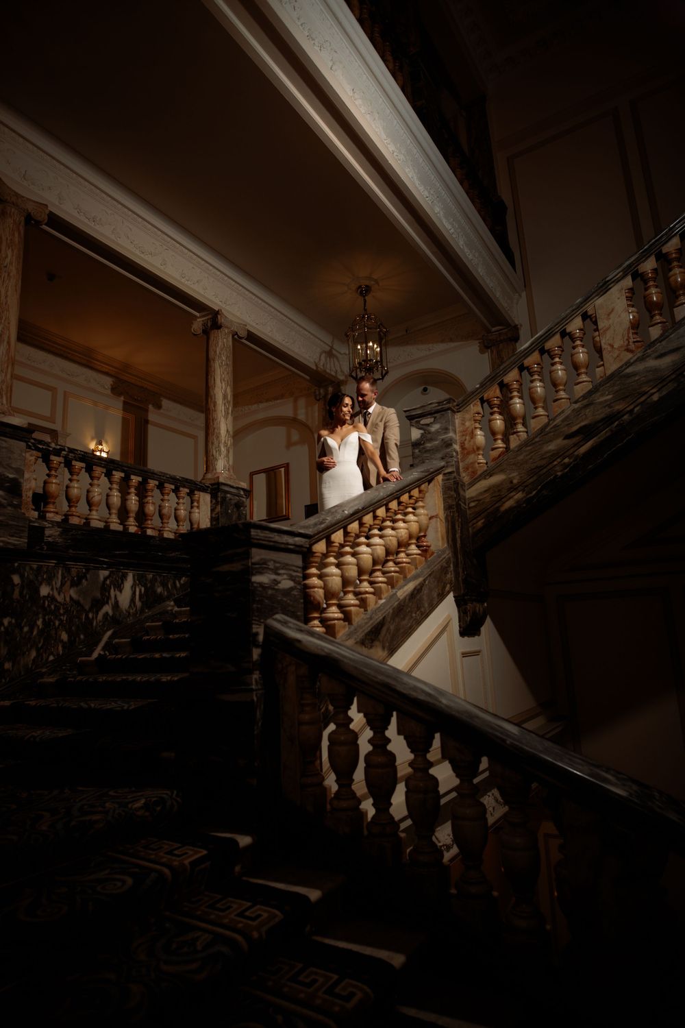 A dramatic moody shot of an ornate vintage wooden staircase in a historic building with dramatic lighting.