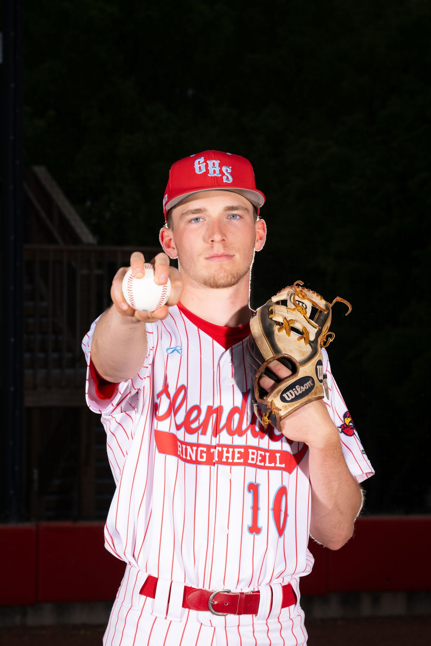 Baseball player in striped uniform holding ball and glove on field at night.