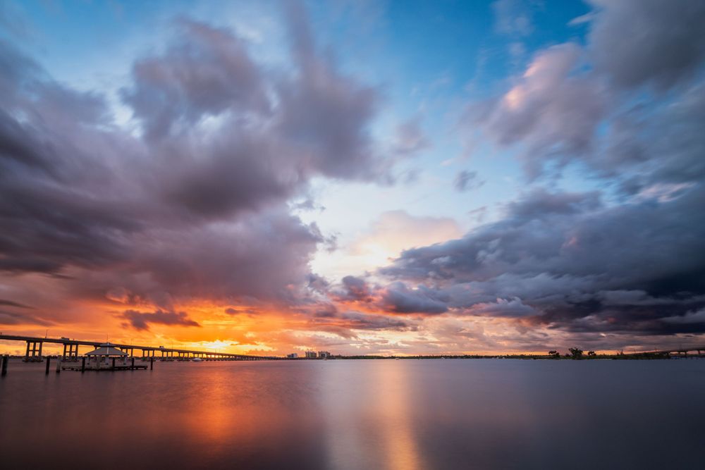 Vibrant sunset over water with silhouetted pier and dramatic purple clouds.