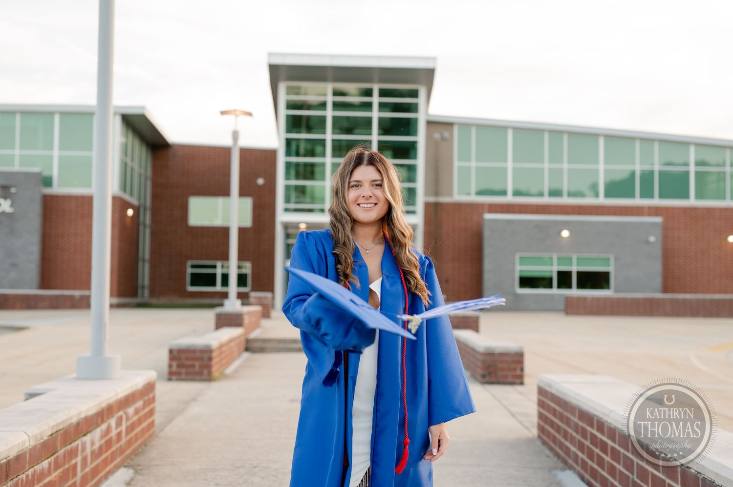 Graduate in blue cap and gown poses confidently outside modern educational building.