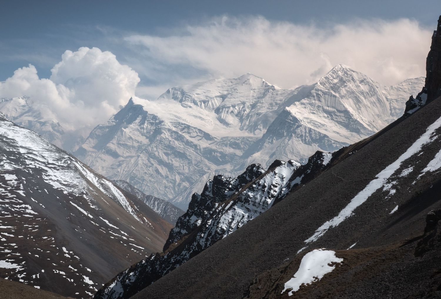 Dramatic snow-capped mountain peaks rise against cloudy skies in a rugged alpine landscape.