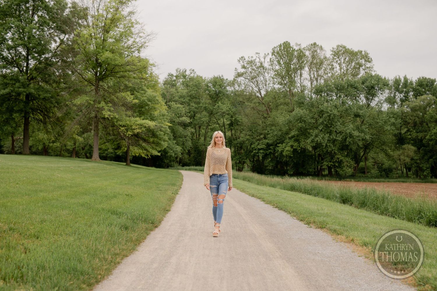Casual spring fashion walking shot on a rural path surrounded by lush greenery.