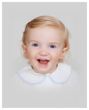 Studio portrait of joyful toddler with blonde hair wearing white collar with blue trim.
