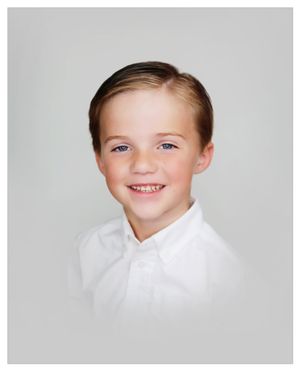 School portrait of happy child in white collared shirt against gray background.