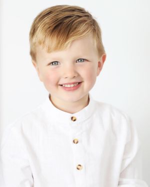A happy child in a white button-up shirt smiles warmly against a clean white background.