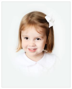 Portrait of young child with white bow accessory wearing white collared shirt.