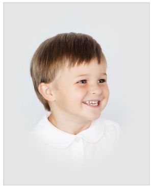 Studio portrait showing child in white collar smiling against light background.