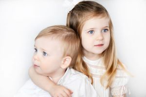 Two children in white outfits pose together against a light studio background.