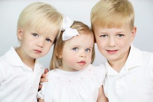 Studio portrait of three siblings in white clothing against light background.