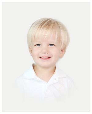 A smiling child in a white polo shirt poses for a bright studio portrait against white background.